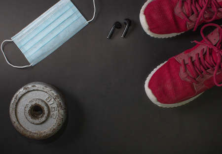 fitness background with red tennis shoes, weight plates and headphones and face mask. concept of sports training in times of pandemicの写真素材