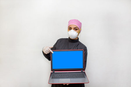 female doctor or dentist in surgical suit and n95 face mask showing laptop screen