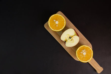 Orange and apple halved on table on blackの写真素材