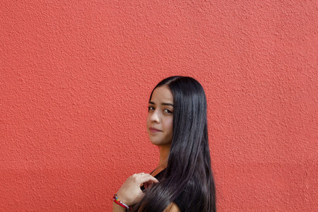 portrait of young mexican woman with long hair on red isolated background