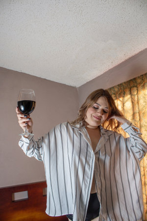 sensual woman dancing happy on the bed with glass of red wineの写真素材