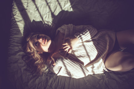 beautiful happy woman with sensual lips lying on the bed with light coming through the windowの写真素材