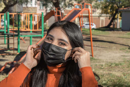 beautiful mexican woman in the park putting on face mask. Hispanic teenagerの写真素材