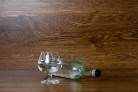 glass and bottle lying down with clear liquor like tequila, mezcal or vodka on elegant wooden backgroundの写真素材