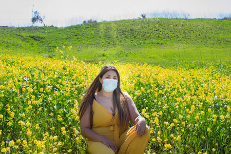 beautiful latin woman wearing facial mask sitting in field full of flowers. new normal