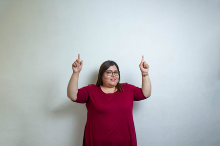 fat woman on isolated background pointing up with both hands, plus size model