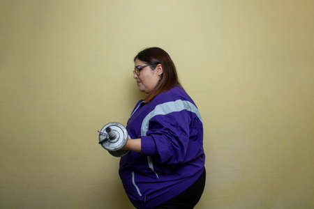 fat woman exercising with dumbbells to lose weight. obese model doing bicep curlsの写真素材
