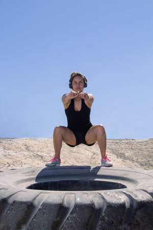 Hispanic fitness woman doing squat on top of tire. workout