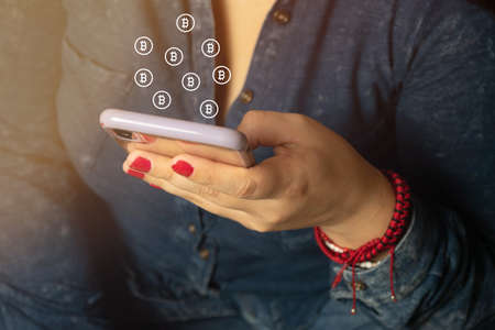 closeup of woman using cell phone to manage her cryptocurrencies, with bitcoin iconsの写真素材