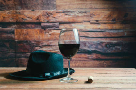 glass of red wine next to cork and fedora hat in cavaの写真素材