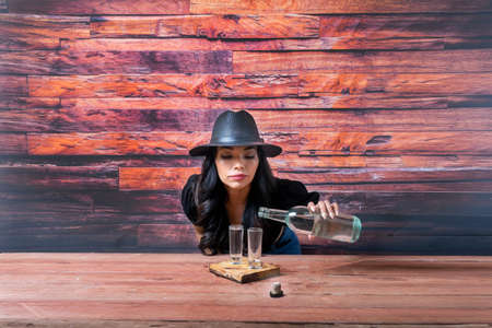 Beautiful and sensual Latin woman wearing fedora hat and serving shots of tequilaの写真素材