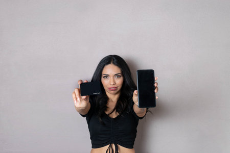 Hispanic woman showing black credit card and cell phone. technology and finance conceptの写真素材