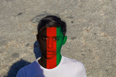 Young man with a sad look with his face painted with the colors of the flag of Afghanistan, concept...