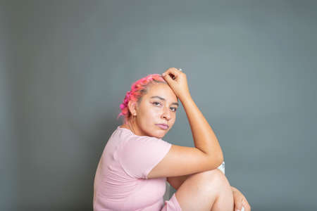fashion portrait of young hispanic woman in pink dress sitting, looking at cameraの写真素材