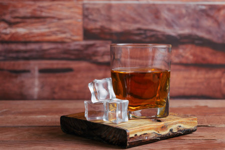 glass of whiskey or cognac on planks with ice cubesの写真素材