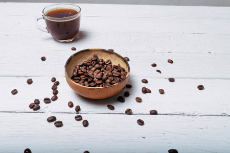 coffee beans in front of cup of coffee on white planks