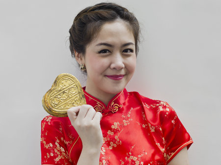 Beautiful asian woman wear cheongsam and holding golden heartの写真素材