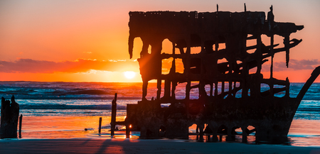 Sun setting behind the wreck of the Peter Iredale on the beach in Fort Stephens State Park, Oregonの写真素材