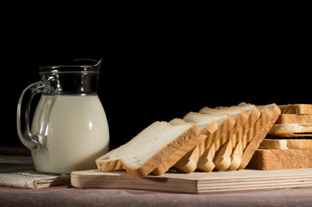 Jar with milk and slices of bread on the table on black background