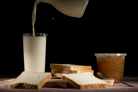 serving milk with slices of bread and jam on the table on black background