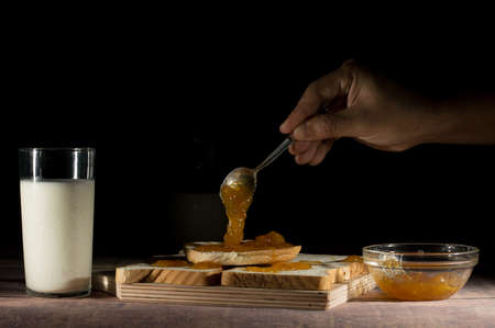 spreading jam on slices of bread with milk on the table on black backgroundの写真素材