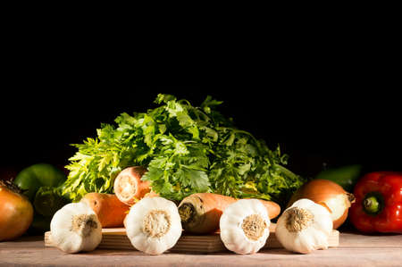 garlic, carrots, onions, peppers and parsley grouped on wooden table on black backgroundの写真素材