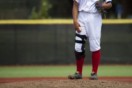 close up of baseball players legs with red stockings standing on first baseの写真素材
