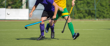 Close up of two field hockey players, challenging eachother for the control and posession of the ball during an intense, competitive match on professional levelの写真素材