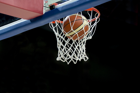 The orange basketball ball flies through the basketの写真素材