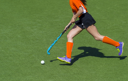 Young hockey player woman with ball in attack playing field hockey gameの写真素材