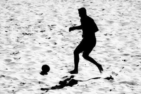 silhouetted  beach soccer action of male player on sandの写真素材