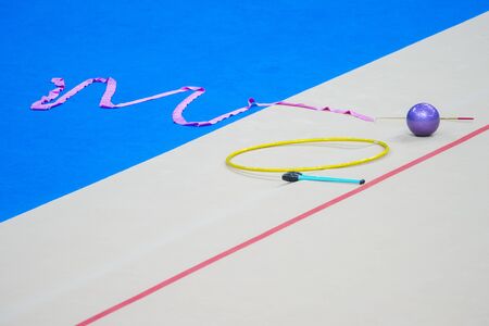 Sports equipment for rhythmic gymnastics lie on the edge of the carpet in the gym. Rhythmic gymnastics clubs, a ball, a hoop.の写真素材
