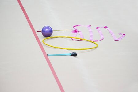 Sports equipment for rhythmic gymnastics lie on the edge of the carpet in the gym. Rhythmic gymnastics clubs, a ball, a hoop.の写真素材