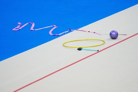 Sports equipment for rhythmic gymnastics lie on the edge of the carpet in the gym. Rhythmic gymnastics clubs, a ball, a hoop.の写真素材