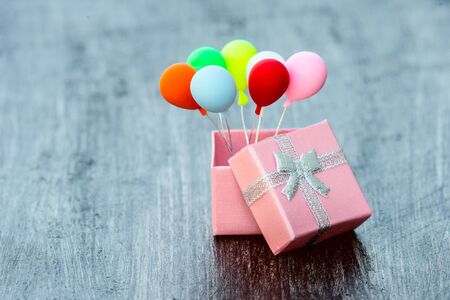Pink gift box with silver ribbon and colorful balloon on wooden background. minimal hollyday conceptの写真素材