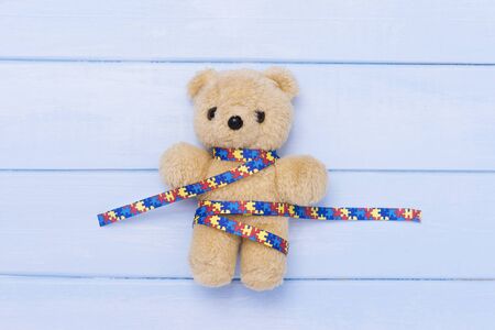 World Autism Awareness day, mental health care concept with teddy bear and ribbon puzzle pattern. On blue backgroundの写真素材