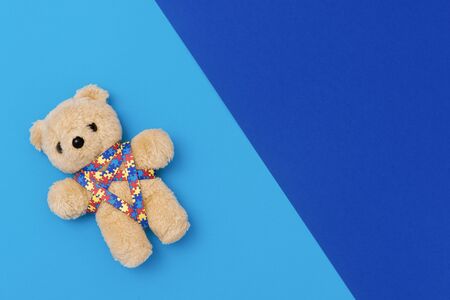 World Autism Awareness day, mental health care concept with teddy bear and ribbon puzzle pattern. On blue backgroundの写真素材