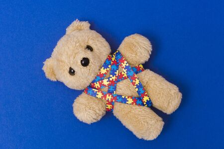 World Autism Awareness day, mental health care concept with teddy bear and ribbon puzzle pattern. On blue backgroundの写真素材