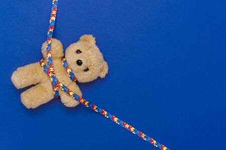 World Autism Awareness day, mental health care concept with teddy bear and ribbon puzzle pattern. On blue backgroundの写真素材