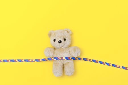 World Autism Awareness day, mental health care concept with teddy bear and ribbon puzzle pattern. On yellow backgroundの写真素材