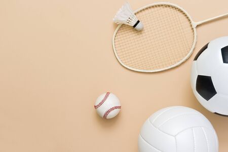 Assorted sports equipment including a basketball, soccer ball, volleyball, baseball, badminton racket on a light brown backgroundの写真素材