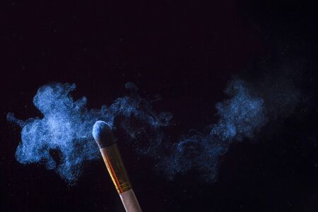 Make-up brush with blue powder explosion isolated on black backgroundの写真素材