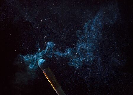 Make-up brush with blue powder explosion isolated on black backgroundの写真素材