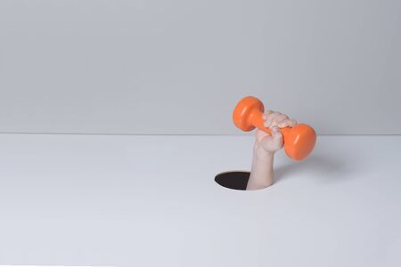 Hand takes a orange plastic dumbbell through torn grey and white paper. Minimalistic sport concept
の写真素材