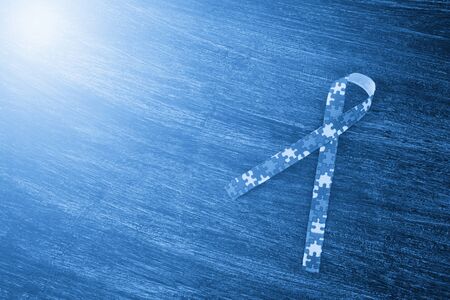 World Autism awareness and pride day or month with Puzzle pattern ribbon on wooden background. Blue filterの写真素材