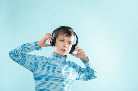 Kid enjoying music on his headphones, listening to music. Handsome young stylish kid in headphones standing against blue backgroundの写真素材