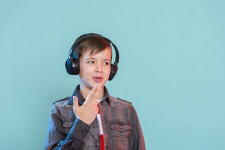 Kid enjoying music on his headphones, listening to music. Handsome young stylish kid in headphones standing against blue background and smilingの写真素材