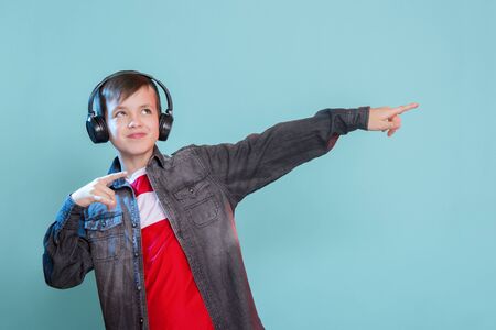 Kid enjoying music on his headphones, listening to music. Handsome young stylish kid in headphones standing against blue background and smilingの写真素材