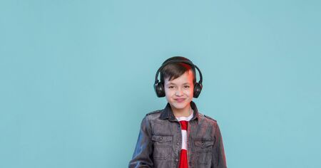 Kid enjoying music on his headphones, listening to music. Handsome young stylish kid in headphones standing against blue background and smilingの写真素材