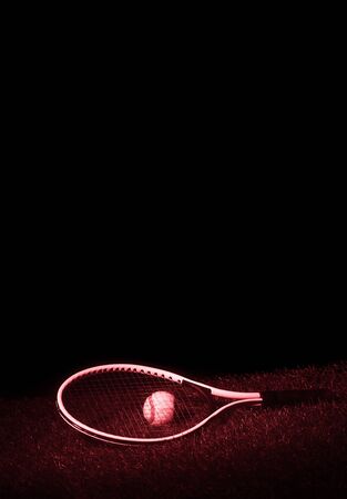 Tennis racket with tennis balls on grass with black background and copy space. Red filterの写真素材